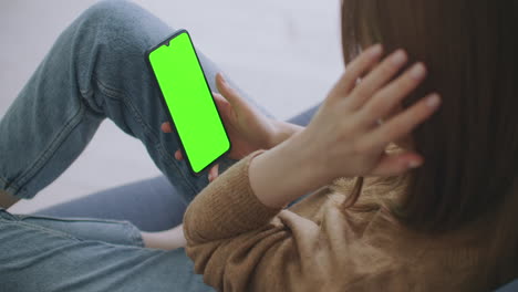Woman-at-Home-Lying-on-a-Couch-using-Smartphone-with-Green-Mock-up-Screen-Doing-Swiping-Scrolling-Gestures.-Guy-Using-Mobile-Phone-Internet-Social-Networks-Browsing.-Point-of-View-Camera-Shot